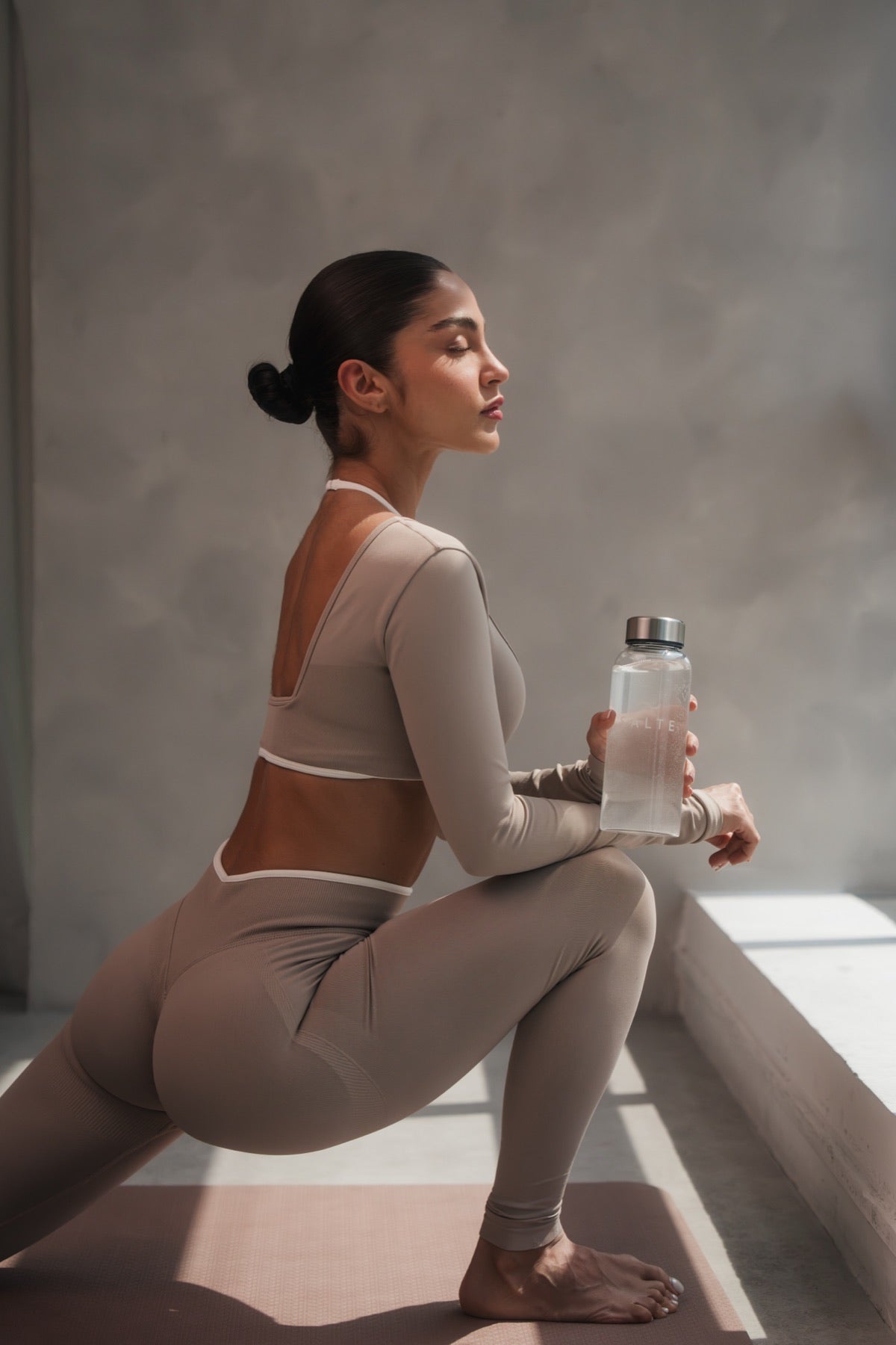 Woman stretching by a sunny window with a SALTE bottle in hand
