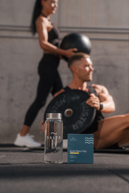 SALTE Lemon electrolytes 30-pack and glass bottle at the gym with athletes training